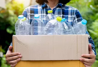 Mujer cargando botellas de plástico en una caja de cartón